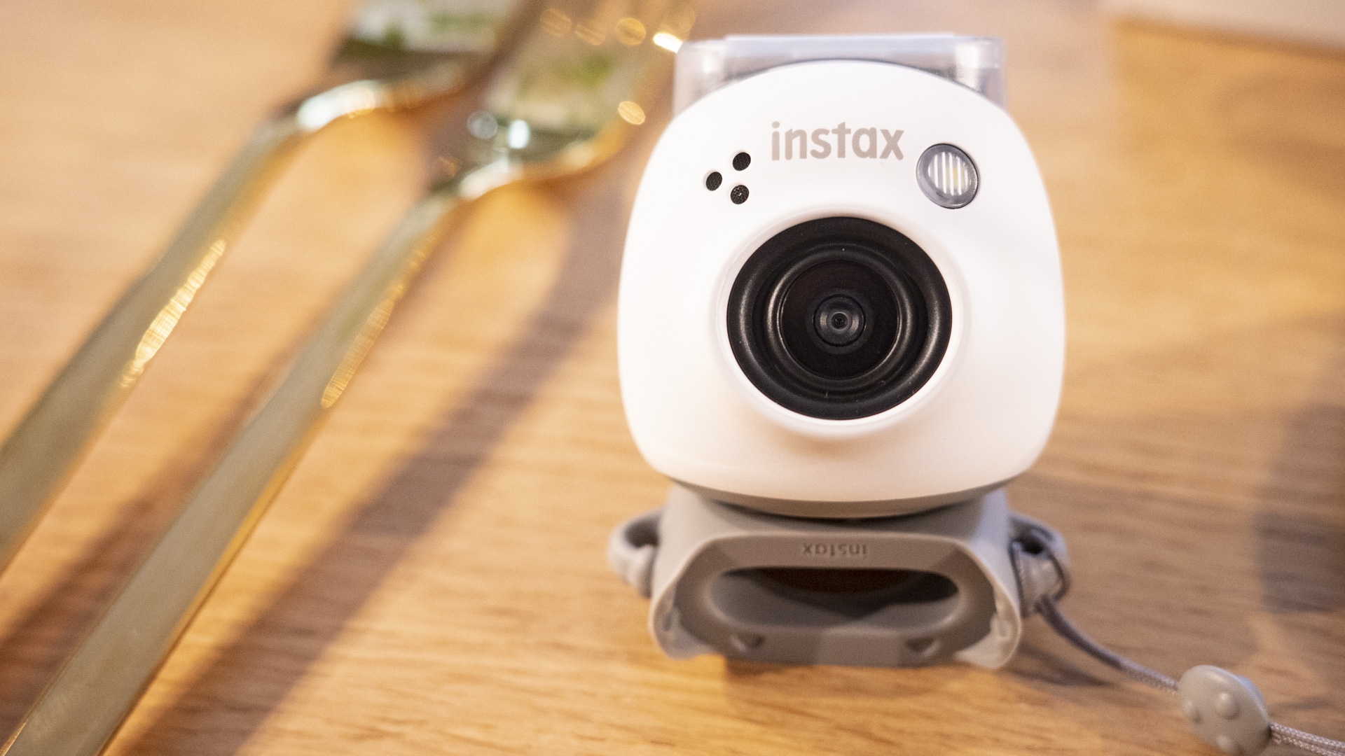 White Fujifilm Instax Pal resting on the detachable ring on a wooden table