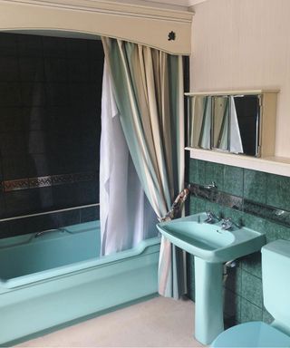 an old fashioned bathroom with blue bath and sink, with a curtain next to the bath