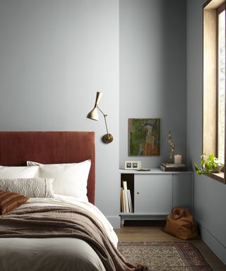 A light blue-gray bedroom with a rust-colored headboard, green painting and large window