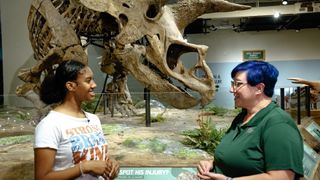 A student host discusses the Triceratops Skeleton behind her. 