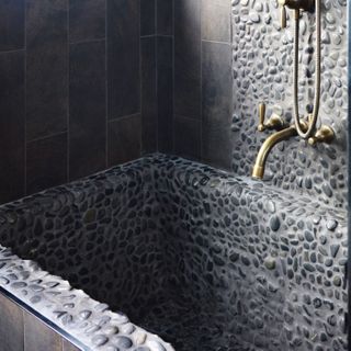 pebbled bath with a bronze shower and taps