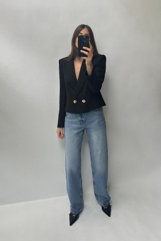 Model takes picture in mirror wearing black blazer, blue jeans and black heels