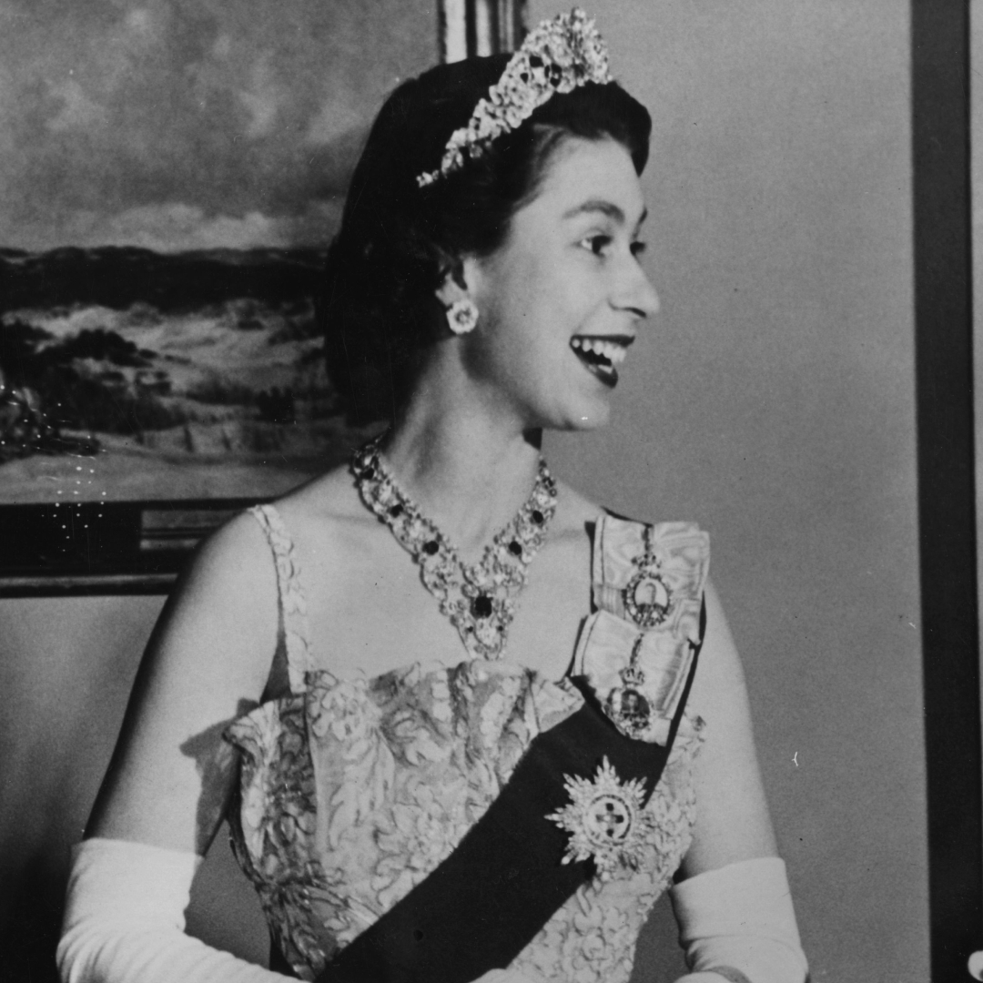 Queen Elizabeth wearing a tiara, gown and sash and laughing