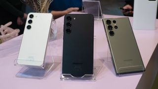 Samsung Galaxy S23 (crème), S23 Plus (zwart) en S23 Ultra (groen) op standaarden naast elkaar