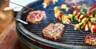 close up shot of a BBQ cooking burgers and vegetable skewers to demonstrate how to BBQ right by using all edges of the grill