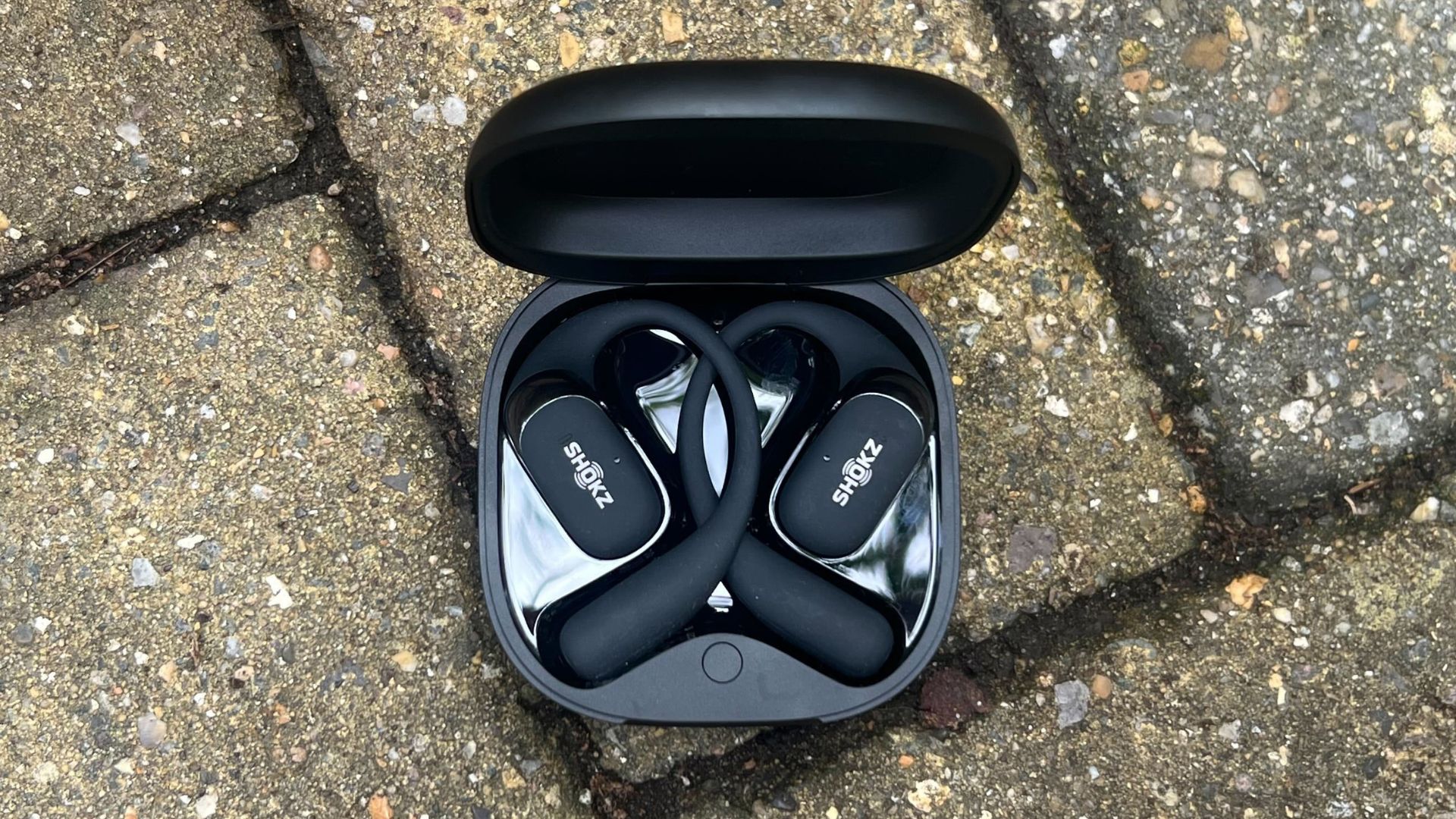 Shokz OpenFit 2+ headphones in case sitting on garden stones