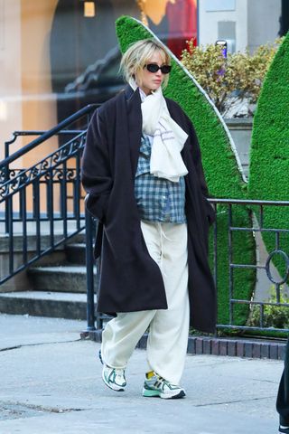 A photo of Jennifer Lawrence going shopping with her husband at The Row's Upper East Side store in New York City, clad in a black coat, New Balance sneakers, and off-white sweatpants.