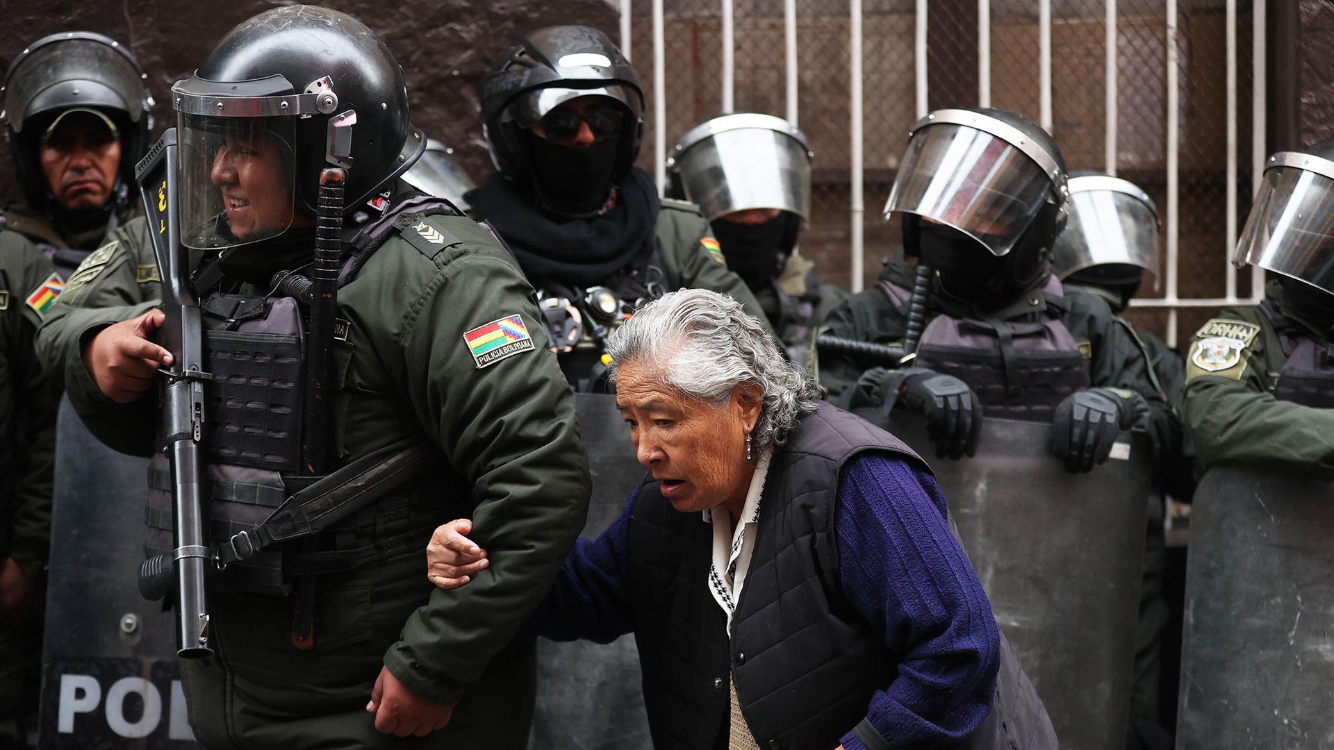 
                                An armed policeman in full riot gear helps an elderly woman past a demonstration in La Paz, Bolivia
                            