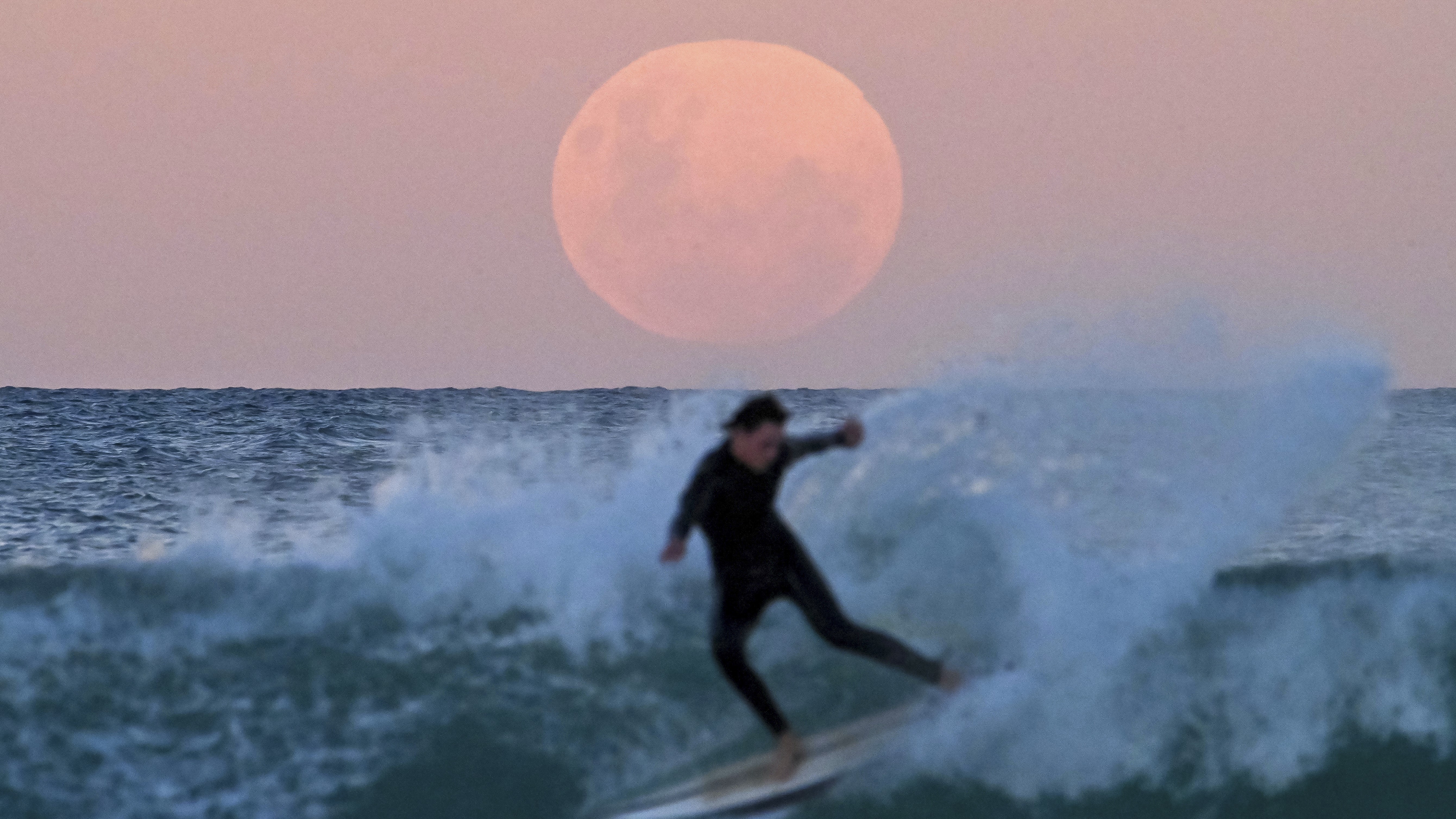 Um surfista da Austrália dá as boas-vindas à lua cheia de 26 de maio de 2021.