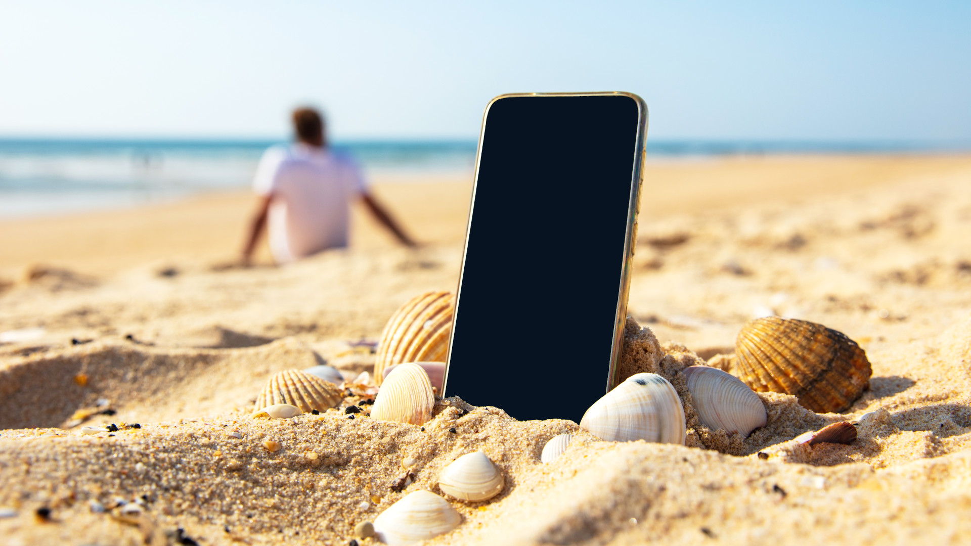 Mobile phone on the beach with a person relaxing in the background