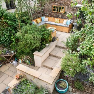 An urban garden with a paved area, plants and wooden benches