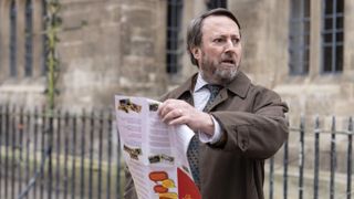 David Mitchell holding a leaflet as John Taylor in Ludwig