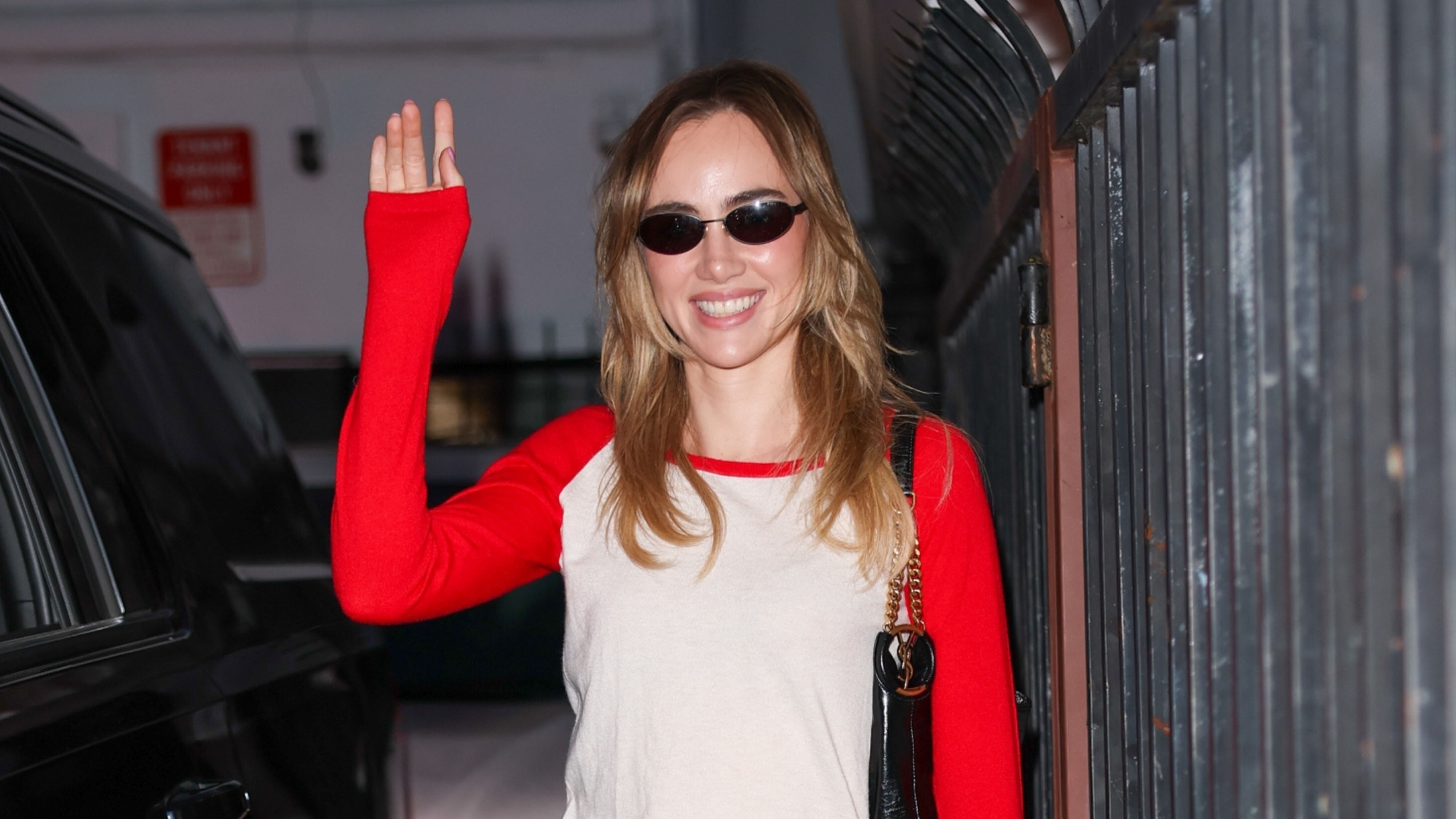 Suki Waterhouse wearing a red and white baseball long-sleeve, printed jeans, and yellow sneakers.