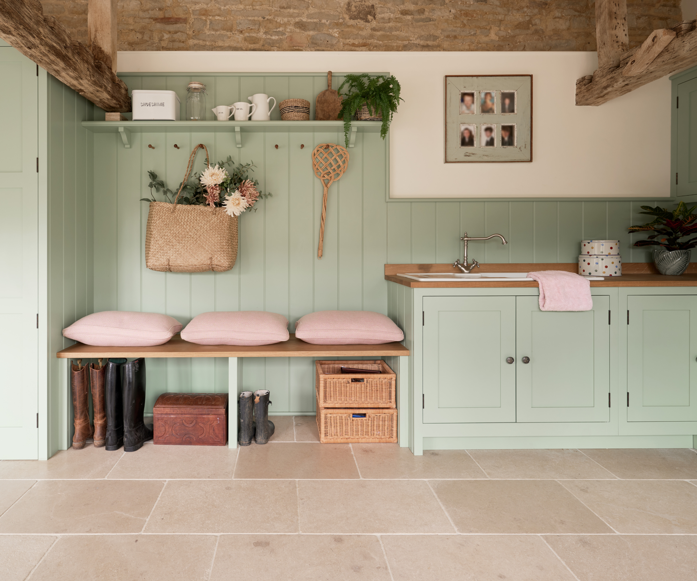 utility room with seating area and shoe storage, fitted with light green cabinets. wall panelling, floor to ceiling cupboards and large floor tiles