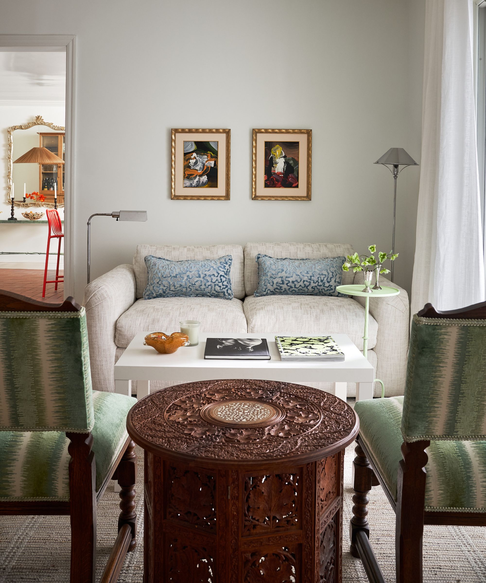 a white living room with texture white sofa, two green striped wooden chairs and an antique Indian side table