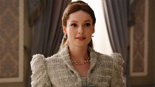 Hannah Dodd with her hair pinned up wearing grey tweed during Bridgerton Season 4. She is standing by a window and staring at the camera.