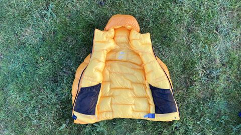 An orange The North Face Summit Series Pumori Down Parka laid open on grass
