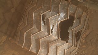One of the aluminum wheels of the Mars Curiosity rover showing a large hole in the tread. 