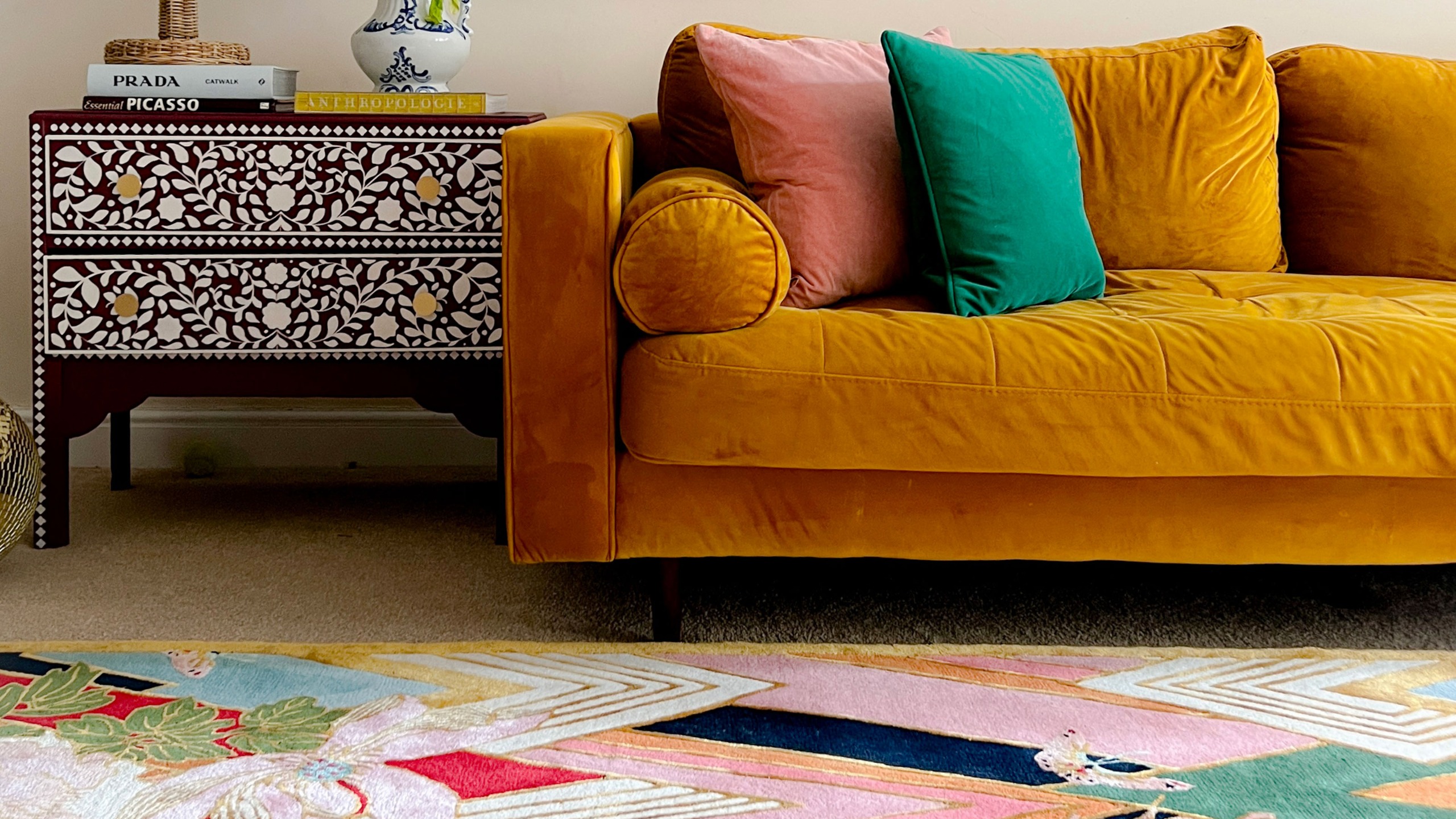 Colourful patterned rug in front of gold sofa and inlaid side table with drawers 