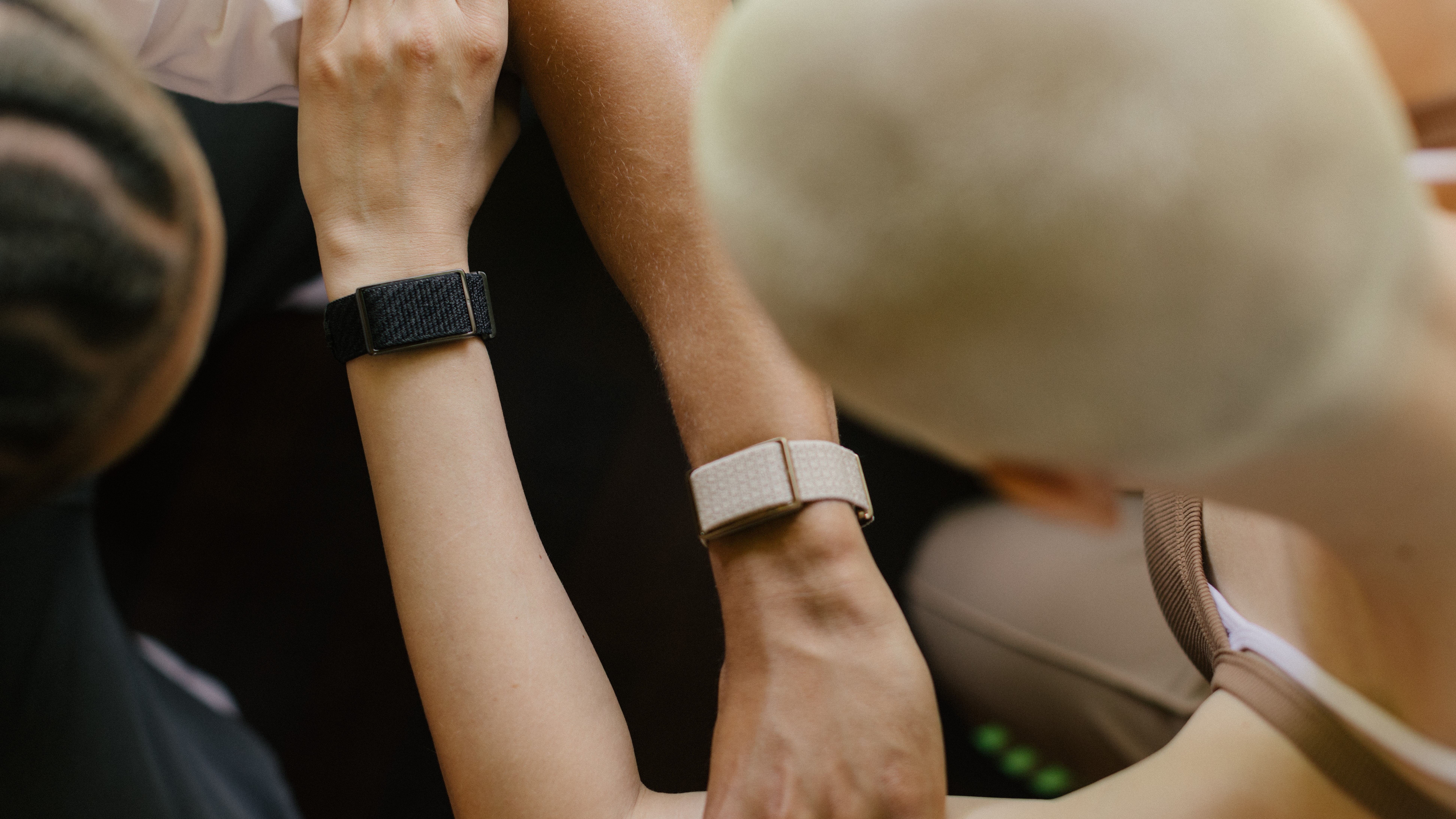 Press photo of two Polar Loop screenless wristbands (one beige, one black) on two different athletes&#039; arms from a top-down perspective, their arms held close together in opposite directions.