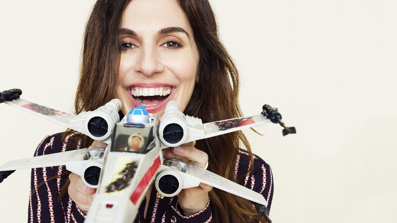 Michelle Rejwan smiles as she holds a toy X-Wing up to the camera