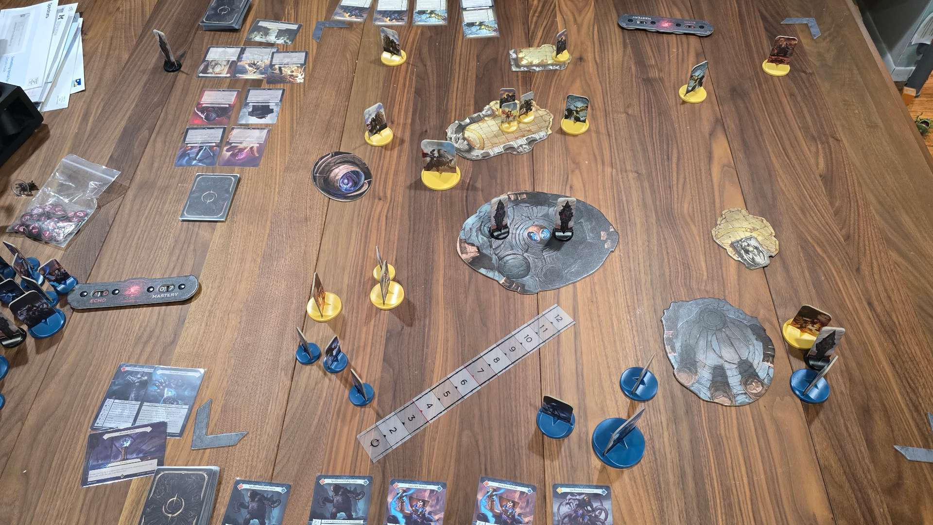 Malediction tokens, terrain pieces, cards, and measurement ruler set up on a wooden table