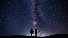 two people with a telescope under the milky way