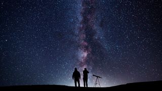 two people with a telescope under the milky way