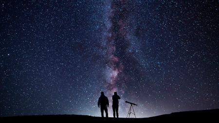 two people with a telescope under the milky way