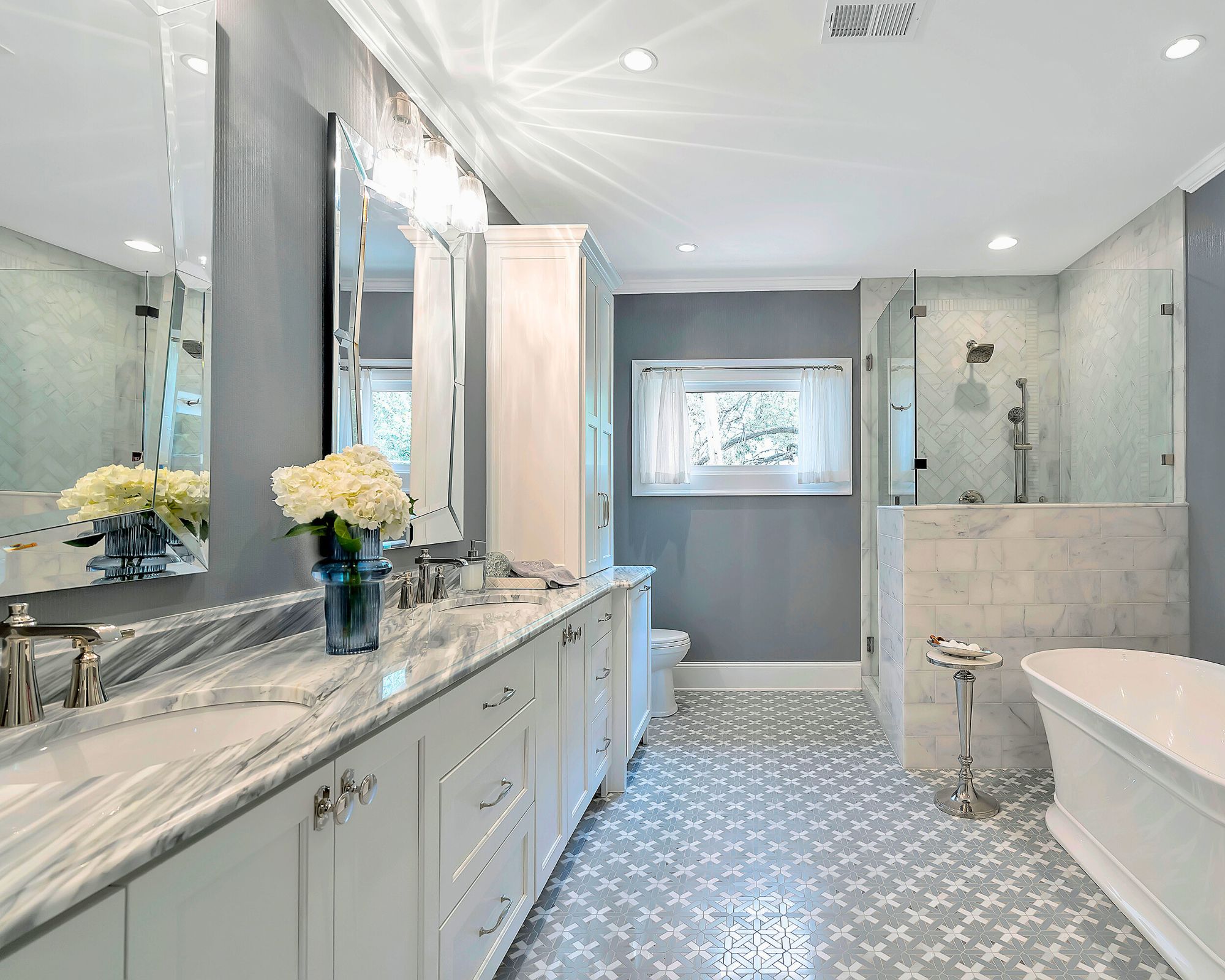 A large gray and white themed bathroom with long marble vanity, freestanding white tub, large walk in shower and mixed tiles