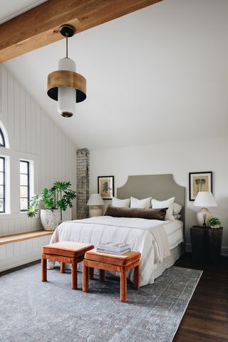farmhouse style bedroom with shiplap wall, arched ceiling, neutral scheme, velvet rust footstools, artwork