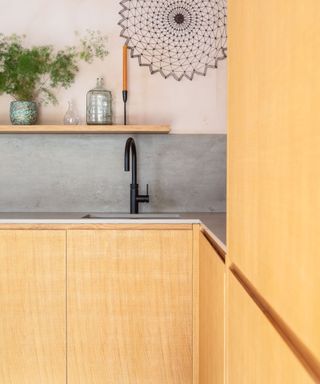 A modern wooden kitchen with neolith beton worktop and pale pink plaster wall