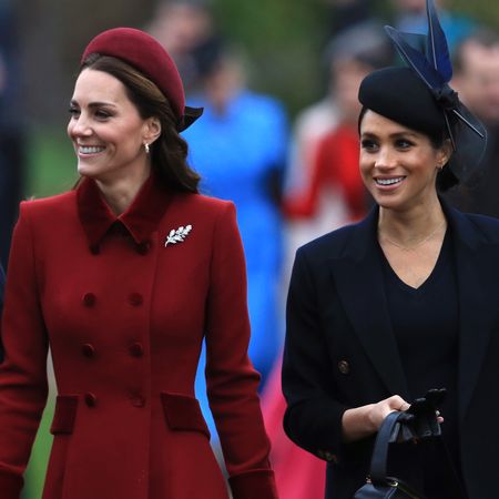 Kate Middleton wears a dark red coat and matching hat while Meghan Markle wears a navy coat and matching hat