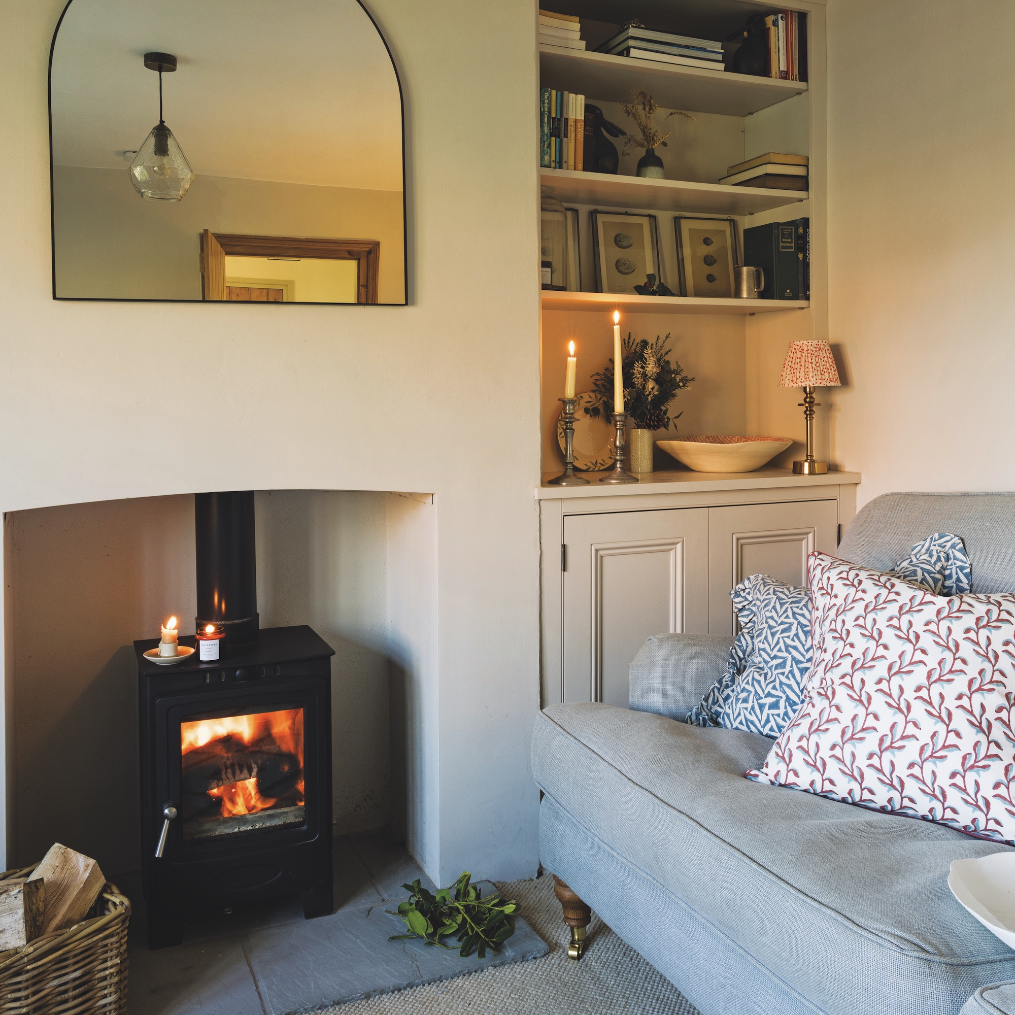 small sitting room snug with white painted walls bookshelves in alcove, blue sofa and woodburning stove in fireplace