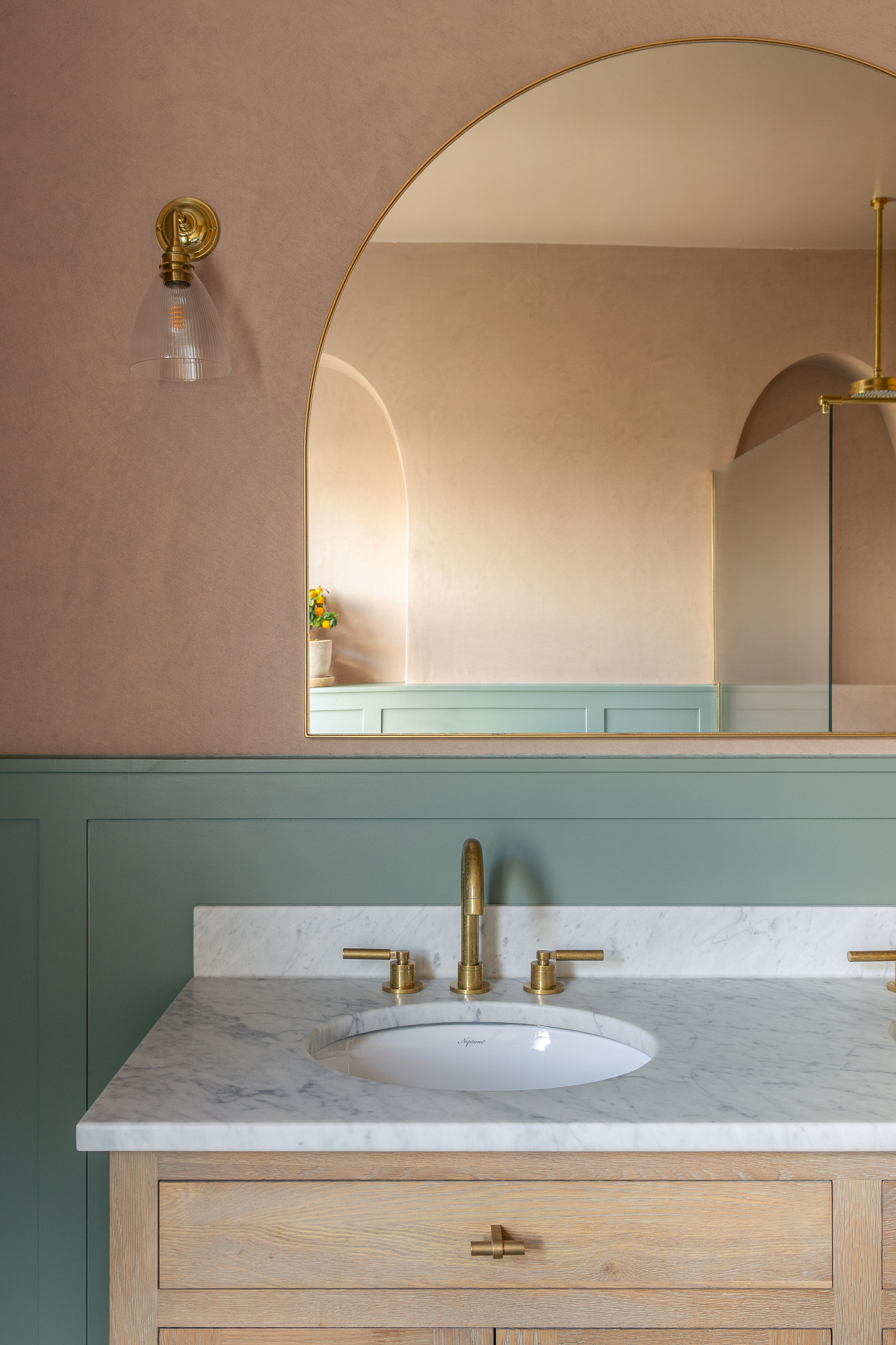 Wooden vanity close-up with white marble countertop, arched mirror, blue painted wood panelling and earthy pink wall