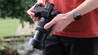 Panasonic Lumix S 28-200mm attached to a camera held in two hands by a person in a red jumper