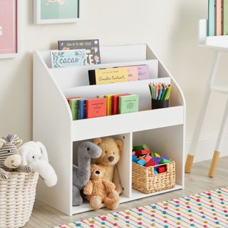 White open storage cabinet with cuddly toys, books and a box of lego pieces, next to basket of teddies