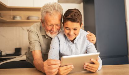 A grandfather and grandson look at a tablet together.