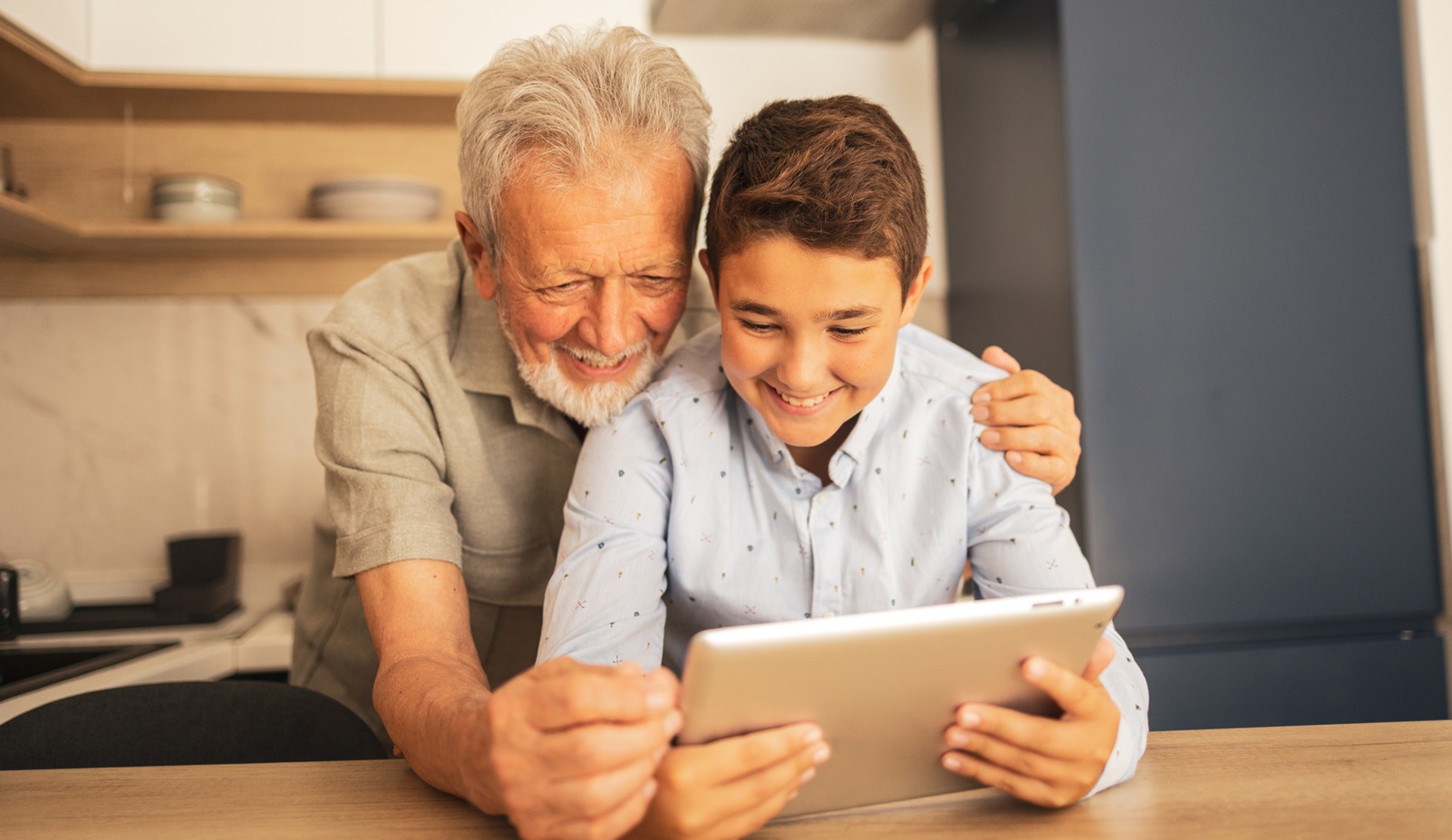 A grandfather and grandson look at a tablet together.