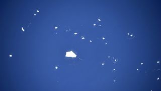 a sea of blue with a couple dozen small white iceburgs floating scattered like dots, with one larger chunk of iceberg near the center