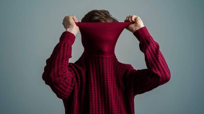 A man hides his face inside a turtleneck sweater in denial.