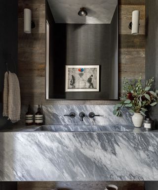 A dark bathroom with a statement stone sink and wood wall paneling