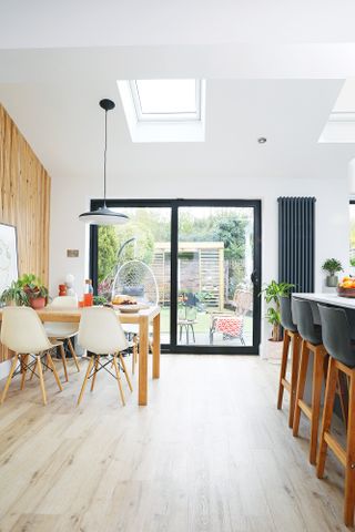 Kitchen-diner with black island and bar stools, oak dining table and white dining chairs, oak slatted panel feature wall and sliding doors leading to garden