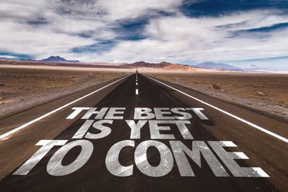"The Best Is Yet to Come" in white, large letters written on a road in the desert.