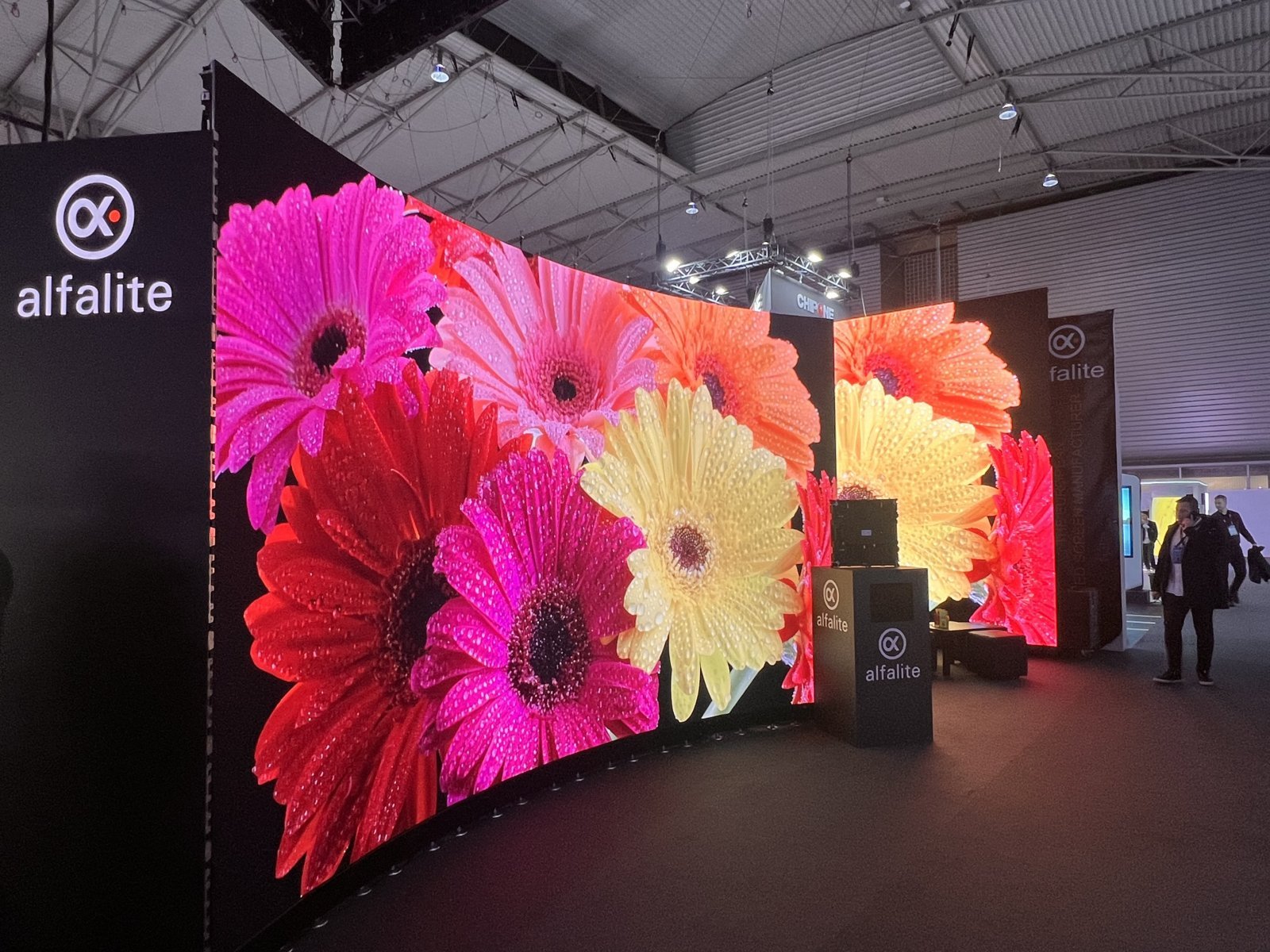 A massive Alfalite LED display shows vibrant pink, yellow, and red flowers.