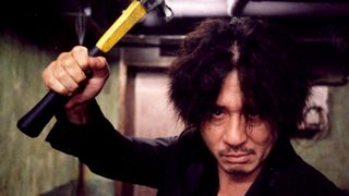 Choi Min-sik as Oh Dae-su staring forward and holding a yellow monkey wrench above his head in the movie Oldboy.