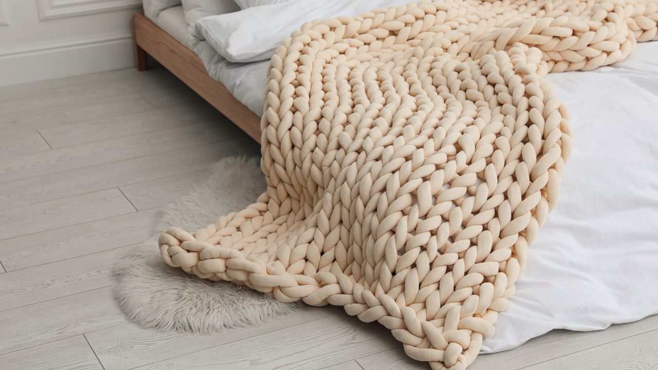 Cream colored chunky knit blanket on white bed