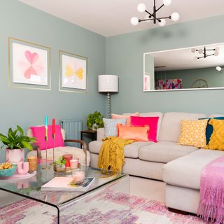 Duck egg blue living room with neutral sofa, colourful cushions and throws, perspex coffee table, sputnik ceiling light, wall mirror, framed artwork