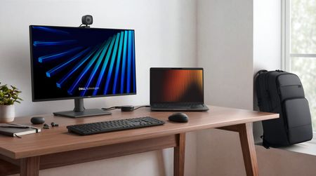 A modern workspace with a large monitor, Dell Pro laptop, keyboard, and mouse on a wooden desk, featuring a potted plant and a black backpack in the background.