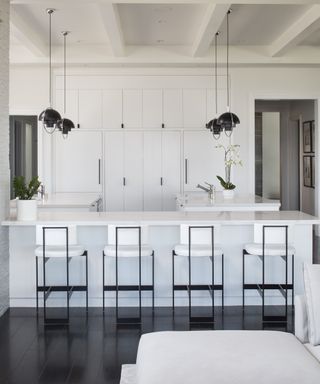 A white kitchen featuring a breakfast bar with a row of black and white stools